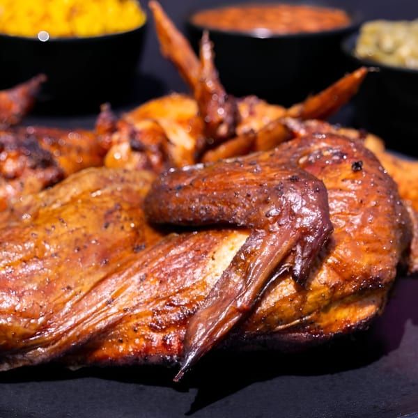 Close-up of a whole roasted chicken with crispy, golden-brown skin, served with sides.