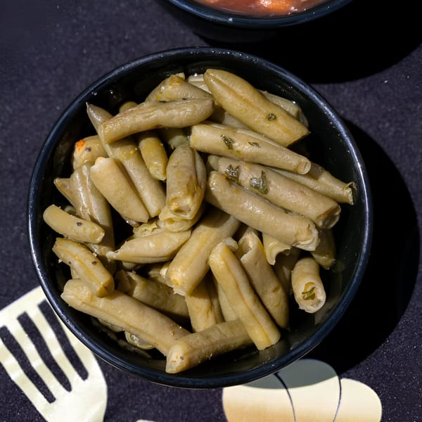 A black bowl filled with cooked green beans, seasoned with herbs, on a dark surface.