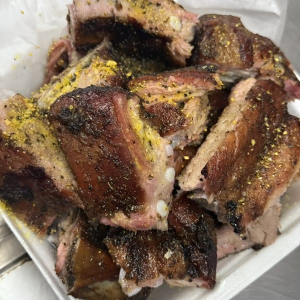 Close-up of Bob's Famous BBQ ribs, seasoned with yellow spices, in a white takeout container.