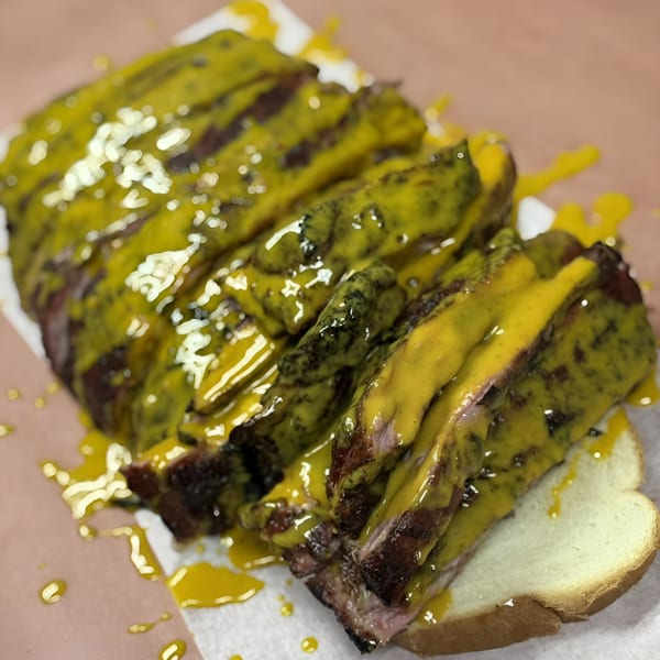 Sliced Bob's Famous BBQ ribs, generously covered in a vibrant yellow mustard-based sauce, served on white bread.