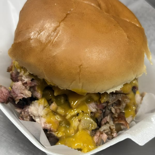 Close-up of a Bob's Famous BBQ sandwich with pulled pork, melted cheese, and onions.